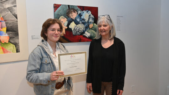 Student Caroline Watts and art teacher Karyn Neubauer pose with Caroline's painting and honorable mention certificate.